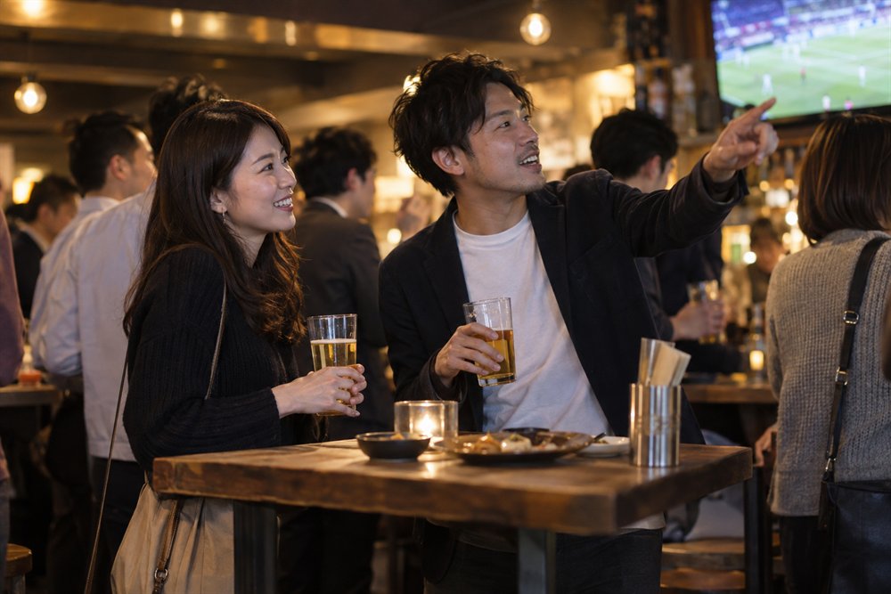 バーの共有テーブルで適度な距離を保ち会話する大人のイメージ